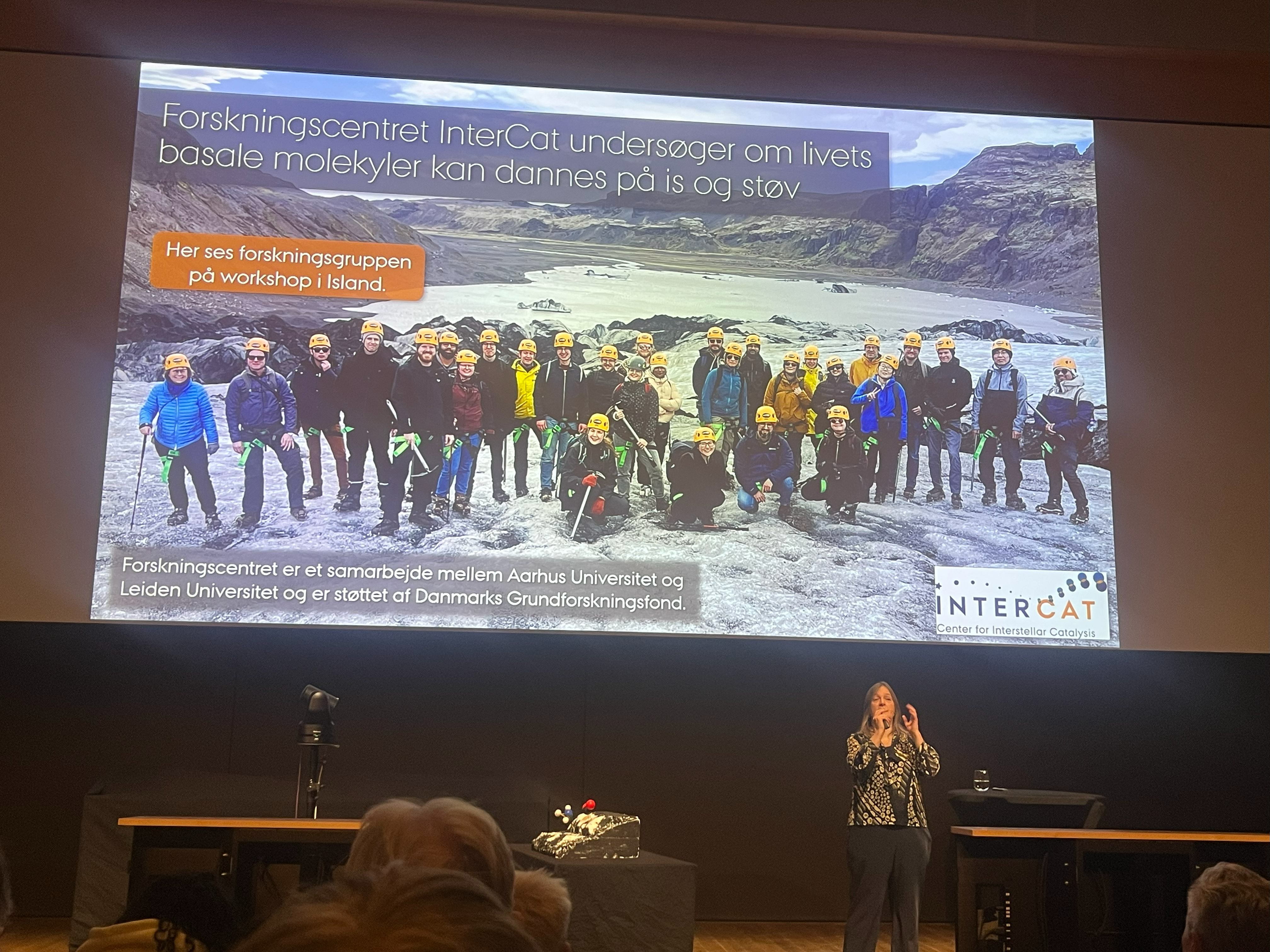 Image of Liv giving talk in front of photo of people on glacier